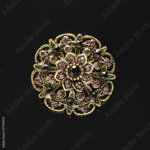 Fotografija copper round brooch with purple diamonds isolated on black