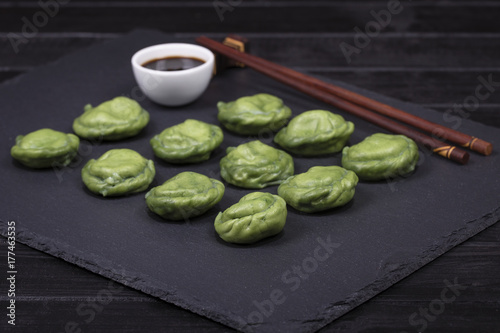 Ukrainian and Russian dishes - green dumplings with beef meat or mashed potatoes or cottage cheese in the dough, together with spirulina on a black slate background