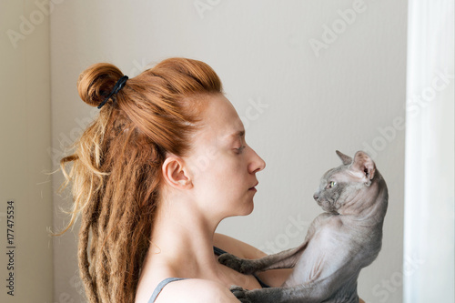 Ginger woman with dreadlocks is holding grey sphynx photo