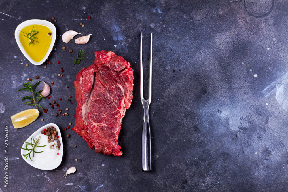 Raw beef steak with spices on dark background with copy space