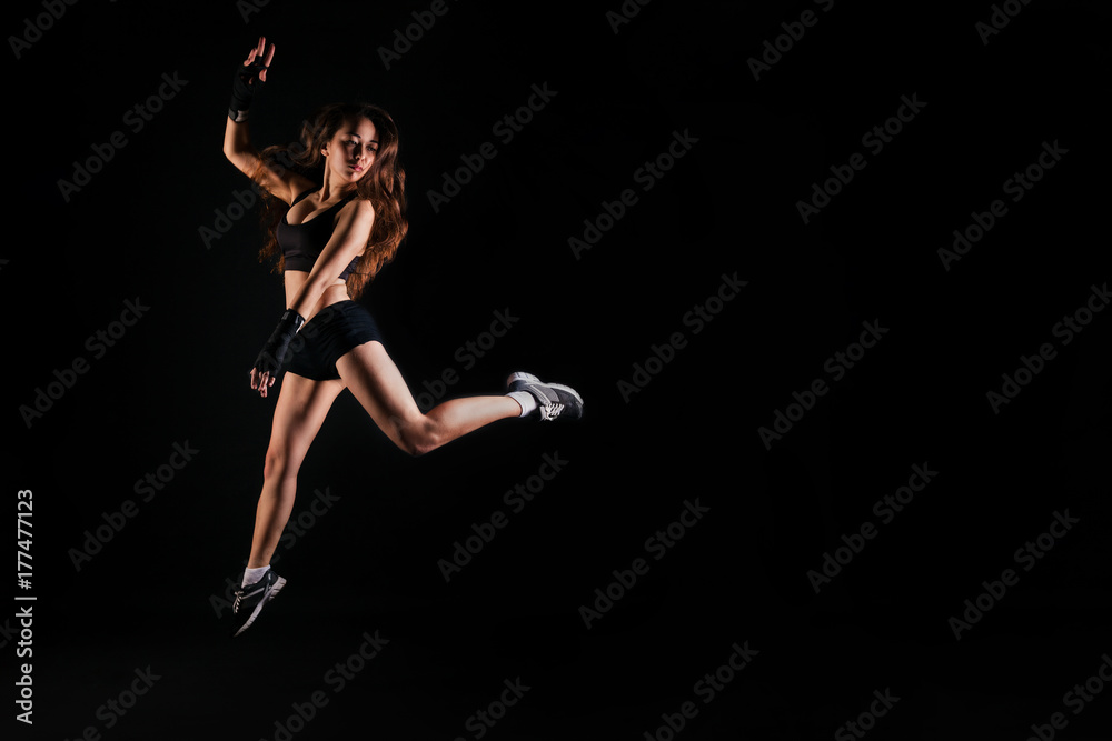 Athletic girl in sport top jumping on black studio background. Fitness concept with copy space.