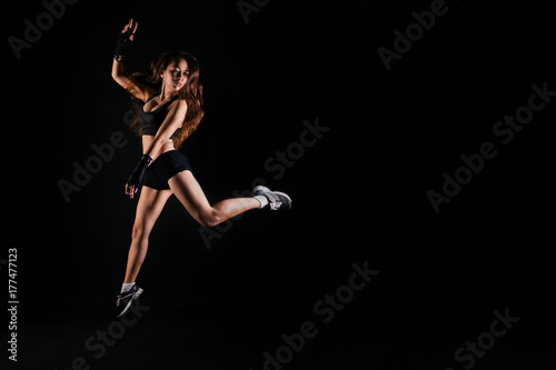 Athletic girl in sport top jumping on black studio background. Fitness concept with copy space.