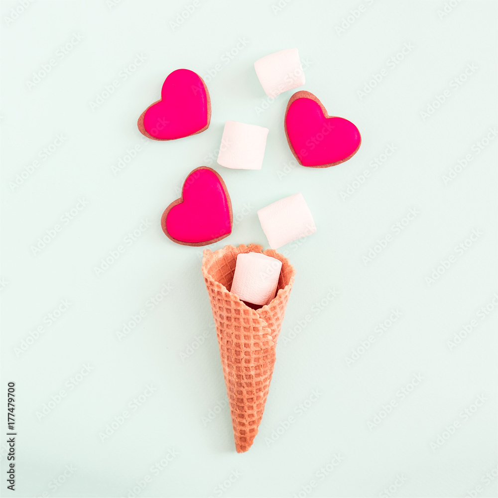 Creative flat lay on pastel blue background. Waffle cone, marshmallows, red heart shaped cookies. Copy space for text Creative flat lay on pastel blue background. Waffle cone, marshmallows, red heart shaped cookies. Copy space for text