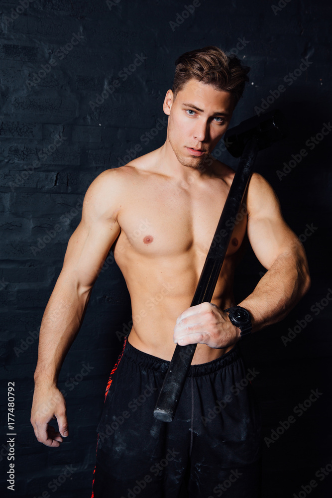 portrait of a young physically fit man workout at gym with hammer. muscular athletic .
