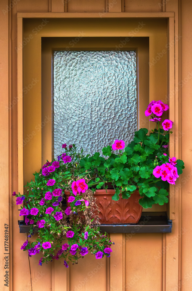 Hut window with flowers.Window of old wooden cabin with a pot with flowers. Hut window with flowers.Window of old wooden cabin with a pot with flowers.