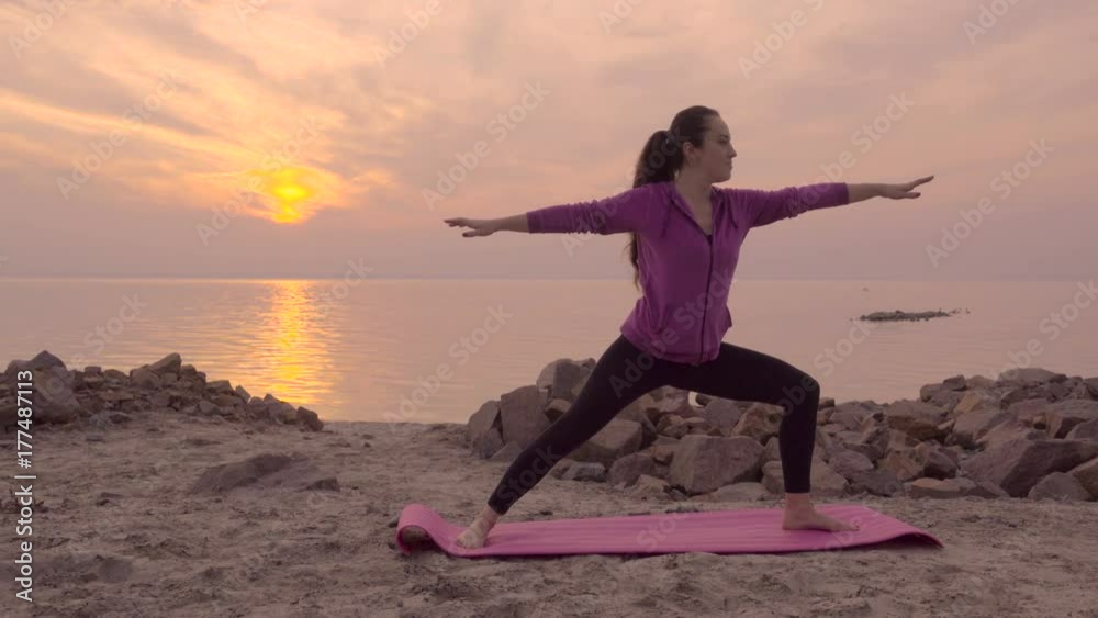 Yoga exercises on the beach with a lot of big stones at sunset. Young sporty woman doing yoga and meditation on seaside. Yoga exercises on the beach with a lot of big stones at sunset. Young sporty woman doing yoga and meditation on seaside.