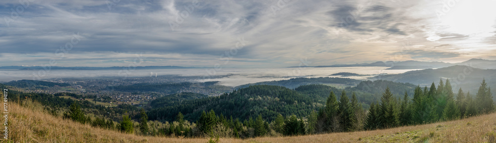 Low fog moves through a small valley town seen at dusk from a hillside overlooking the wide valley.