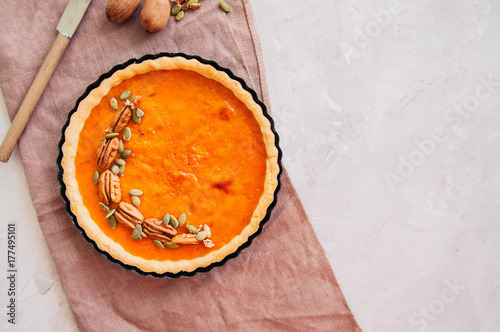 Traditional american baking - Pumpkin pie garnished with pecans and seeds on a white stone background