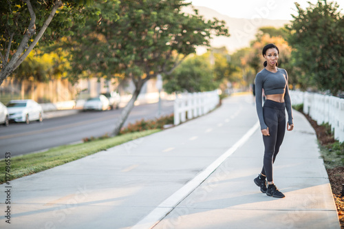 A sporty African American girl standing on a bike path in the city park.
