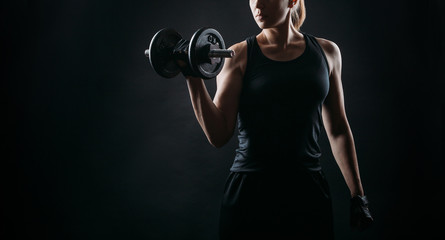 girl exercising squatting with dumbbell on black background with copy space