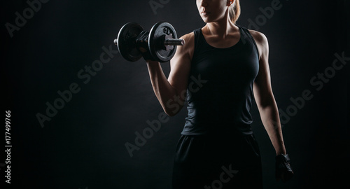 Fotografie girl exercising squatting with dumbbell on black background with copy space