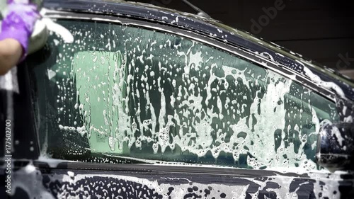 Woman worker washing car with sponge on a car wash