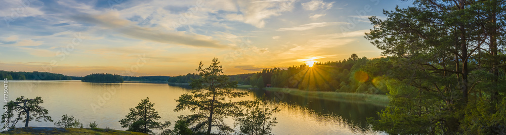 Panorama picture taken in Sweden with sunset over a lake and beautiful glow from the sun - obrazy, fototapety, plakaty 