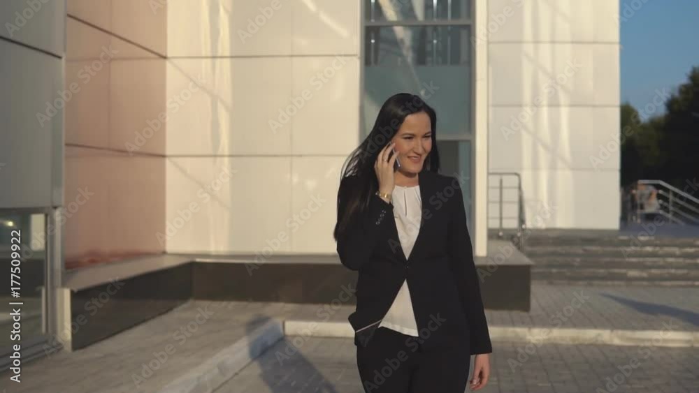 Businesswoman in formal suit talking on smartphone on sunny day against the backdrop of office center Businesswoman in formal suit talking on smartphone on sunny day against the backdrop of office center