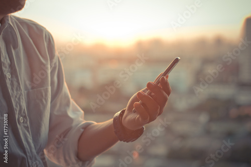 business man using a touch screen smart phone hands in sunset sky on blurred urban city as background, vintage colors