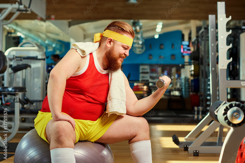 Stockfoto med beskrivningen Fat funny man with dumbbells in the gym. |  Adobe Stock