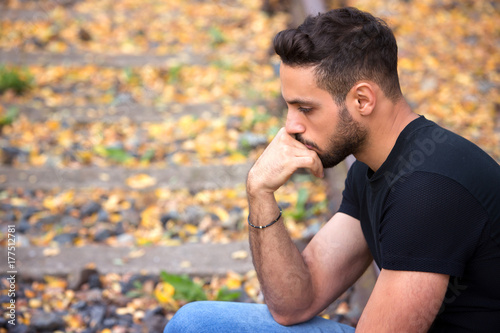 Bild auf Leinwand handsome man sitting on train tracks and looking pensive