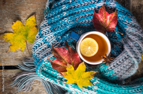 Autumnal concept with cup of tea with lemon, cinnamon stick and anise star on rustic wooden background full of bright yellow leaves