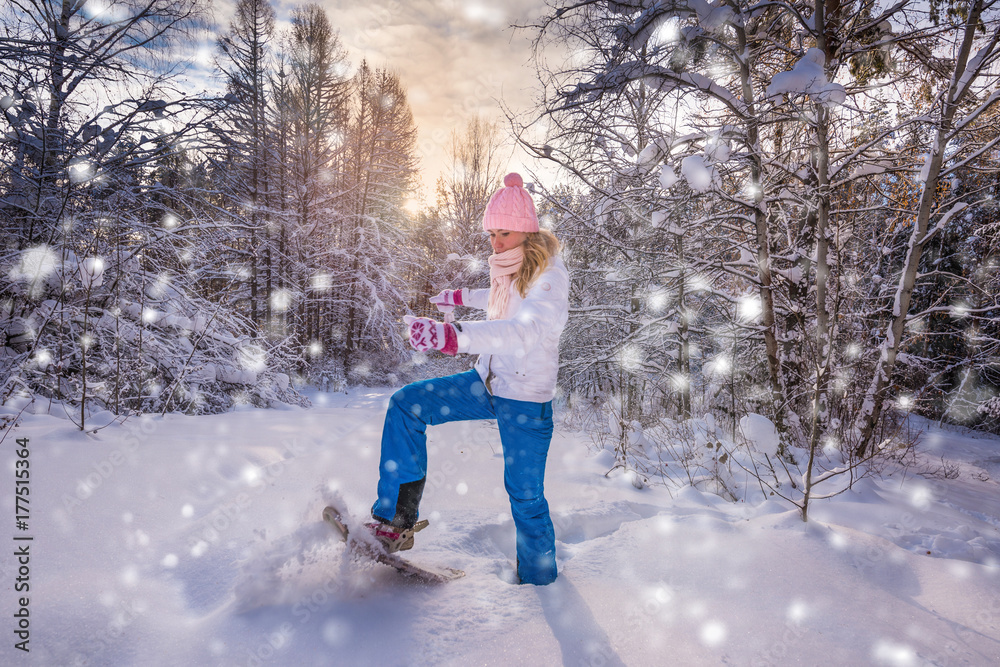 Winter sport activity. Woman with snowshoes on fluffy snow in forest. Beautiful landscape with coniferous trees and white snow. Post processing snowflakes effect