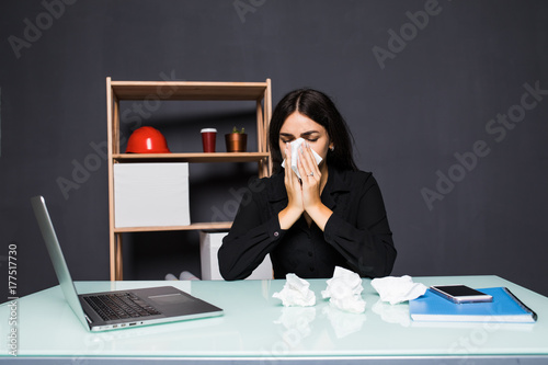 Sick woman sitting at her workplace in the office. A woman blows her nose in the workplace. photo