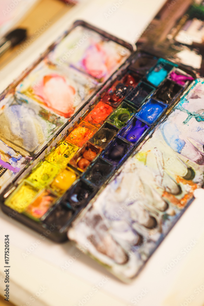 Details of the creative process of the artist, a palette with watercolor paints, brushes and canvas with a sketch.