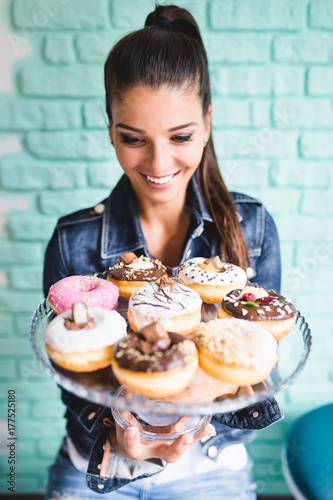 Beautiful young woman enjoying in delicious glazed and decorated donuts. Selectiv focus.