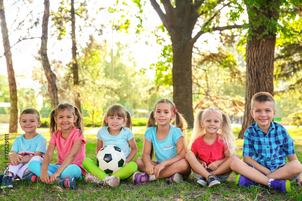 Cute little children with ball sitting on green grass in park Cute little children with ball sitting on green grass in park
