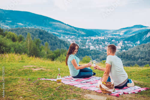 Couple in love on a white and red plaid in a field on a picnic. against a background of a mountains. romantic moment. Man and woman with champagne glass.