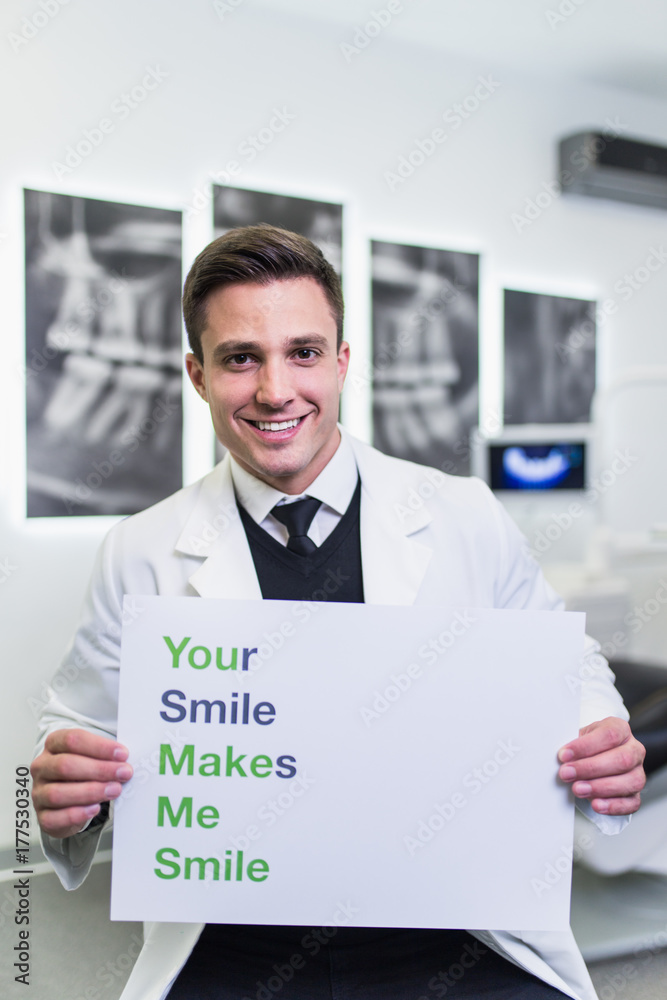 Portrait of handsome smiling dentist posing in his stomatology office and holding pamphlet . Portrait of handsome smiling dentist posing in his stomatology office and holding pamphlet .