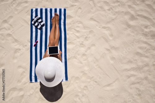 Summer holiday fashion concept - tanning woman wearing sun hat at the beach on a white sand shot from above