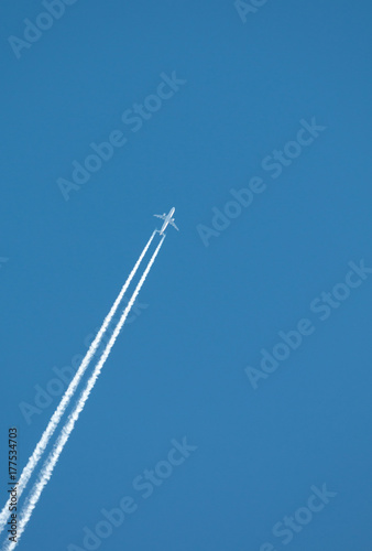 Airplane flying at high altitude leaving its white wake over blue sky