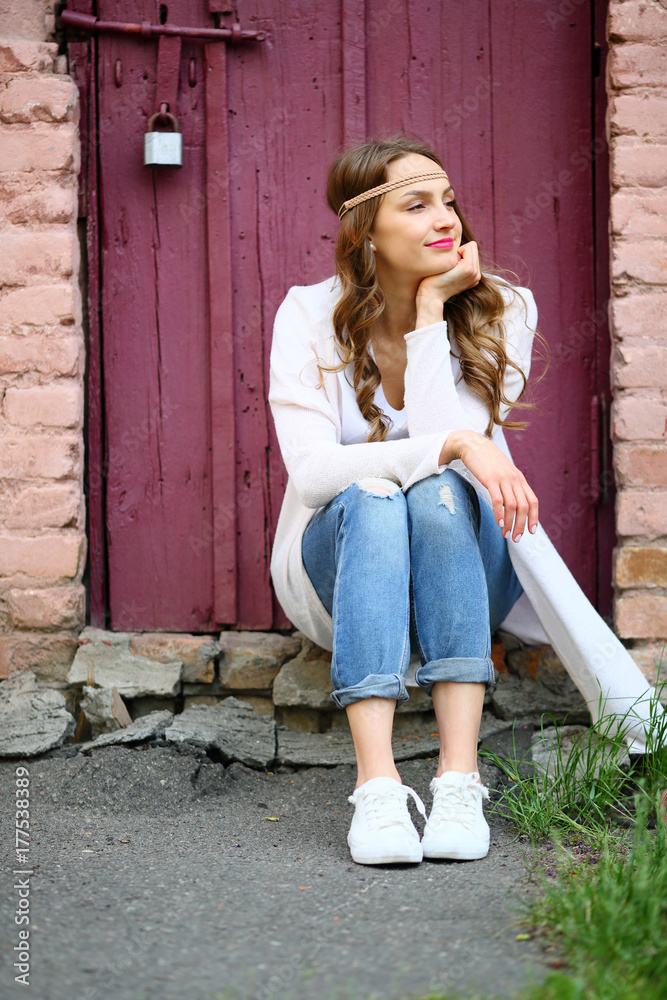Lifestyle moment,hippie woman sitting looking away in beautiful street place, puffy background , pink, wooden door burgundy
