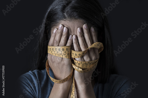 hands wrapped in tailor measure tape covering face of young depressed and worried girl suffering anorexia or bulimia nutrition disorder photo