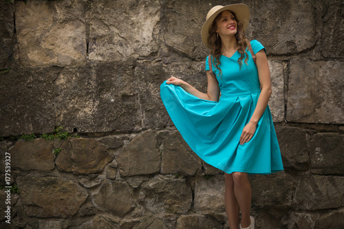 Beautiful smiling young woman in dress, standing near stone background, medieval city