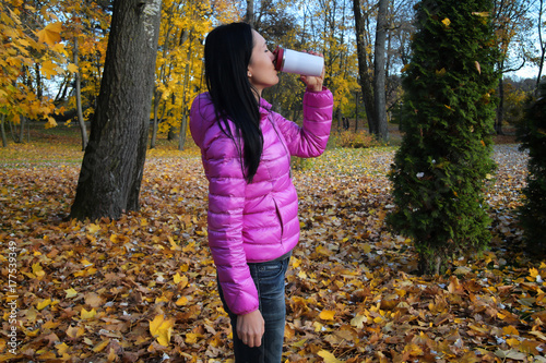 woman drinks from a thermo mug in an autumn park