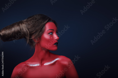 Close up horizontal portrait of a girl in a high fashion, beauty style with red skin, black lips make up at dark background. Devil makeup fashion art design. Halloween holiday concept