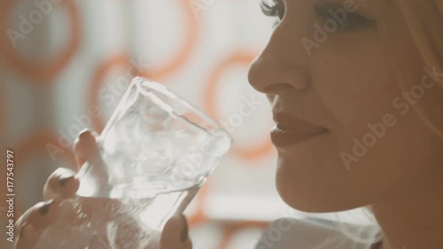 Close-up of the attractive blonde who drinks water from transparent glass beaker