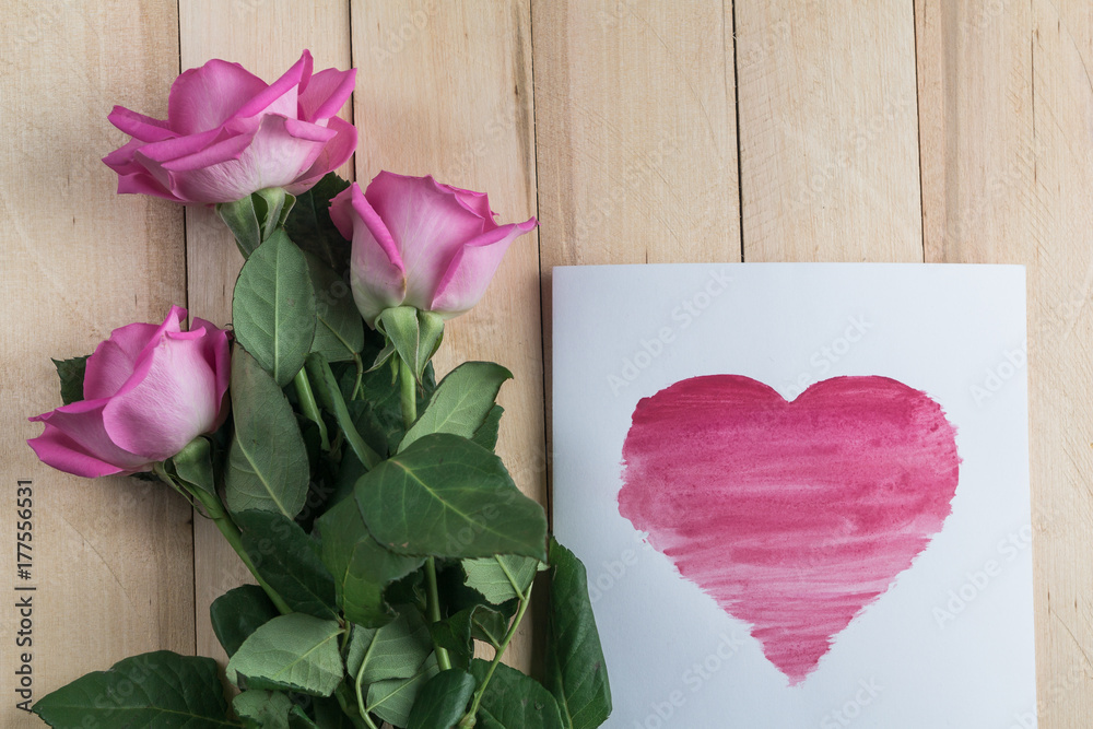 card with a heart and three roses on wooden background