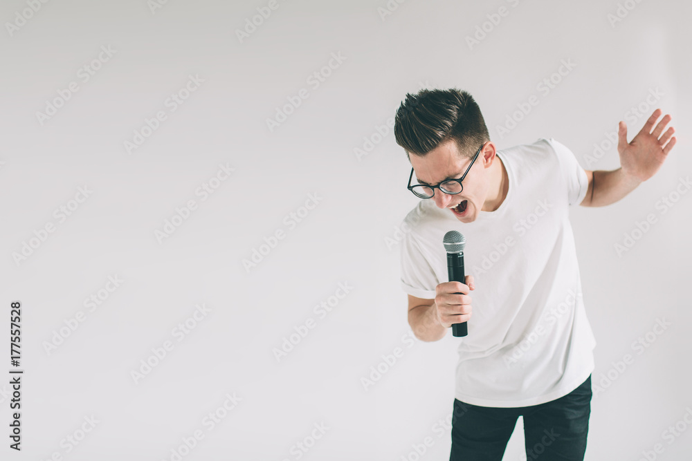 Boy Rocking Out. Image of a handsome man singing to the microphone, isolated on light. Emotional portrait of an attractive guy on a gray background. Nerd is wearing glasses.