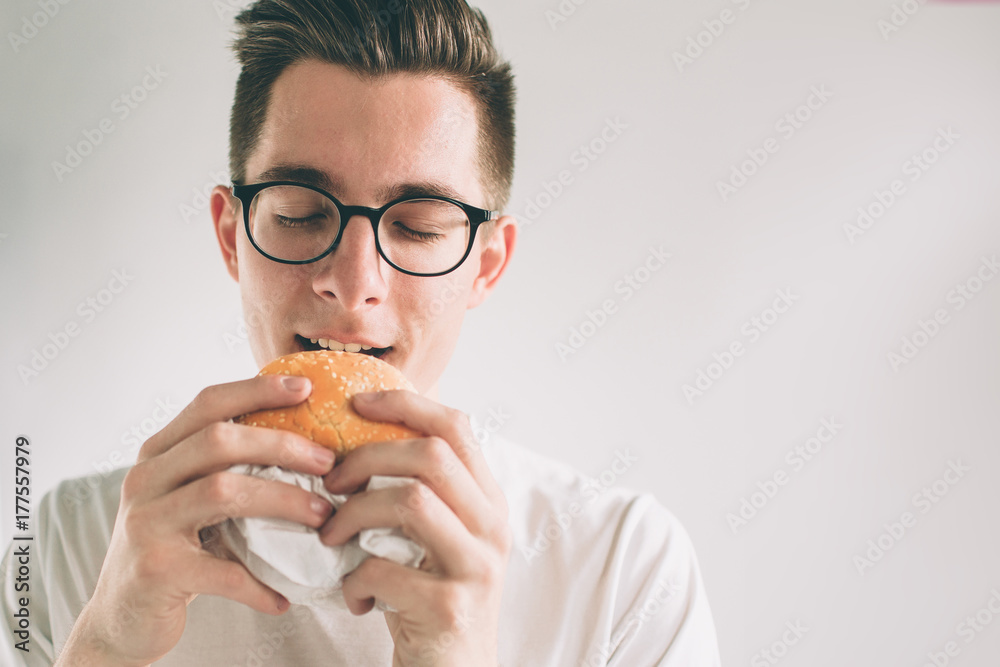 man holding a piece of hamburger. student eats fast food. not helpful food. very hungry man. Nerd is wearing glasses. man holding a piece of hamburger. student eats fast food. not helpful food. very hungry man. Nerd is wearing glasses.