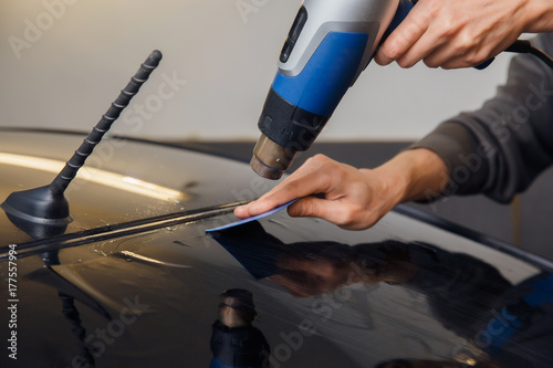 Master installs a tint film for the car glass with a hairdryer and spatula with glare of light. Concept tinting car