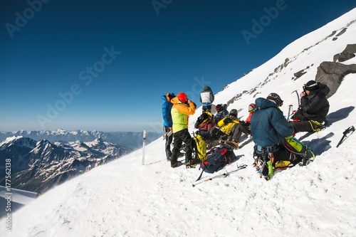 fully equipped Professional mountaineers on a stop sit on a snowy slope in sunny weather.