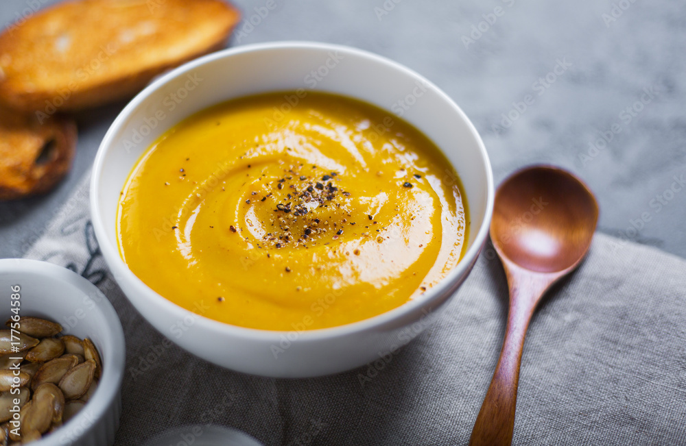 Roasted pumpkin and carrot soup with black pepper and pumpkin seeds on grey concrete background. Close up. Side view. Copy space Roasted pumpkin and carrot soup with black pepper and pumpkin seeds on grey concrete background. Close up. Side view. Copy space