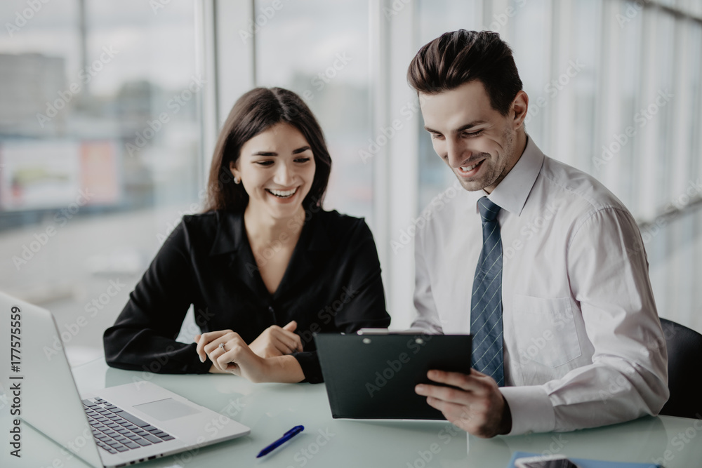 Two entrepreneurs sitting together working in an office desk comparing documents. Office work. Two entrepreneurs sitting together working in an office desk comparing documents. Office work.