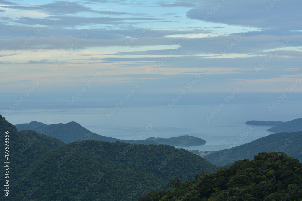 Vista de Ubatuba de cima da Serra do Mar, com camadas de montanhas azuis que acabam no mar. 