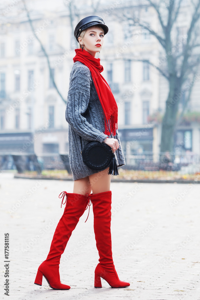 Outdoor full body portrait of young beautiful fashionable woman wearing  trendy cap, red high, over knee boots, stylish clothes and accessories.  Model walking in street. Elegant outfit. Female fashion foto de Stock