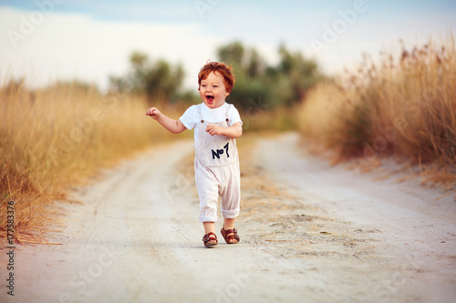 cute toddler baby boy running along the path at summer field