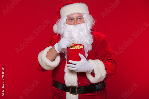 Traditional Santa Claus watching TV, eating popcorn. Christmas. Red background. emotions fear surprise