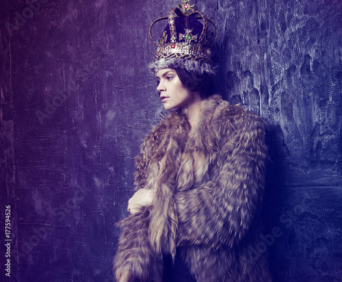 Studio shot of beautiful young woman in crown  and fur coat  at dark studio background © EVGENY FREEONE