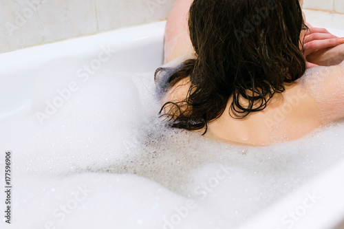 Back view of beautiful young woman enjoying pleasant bath with foam